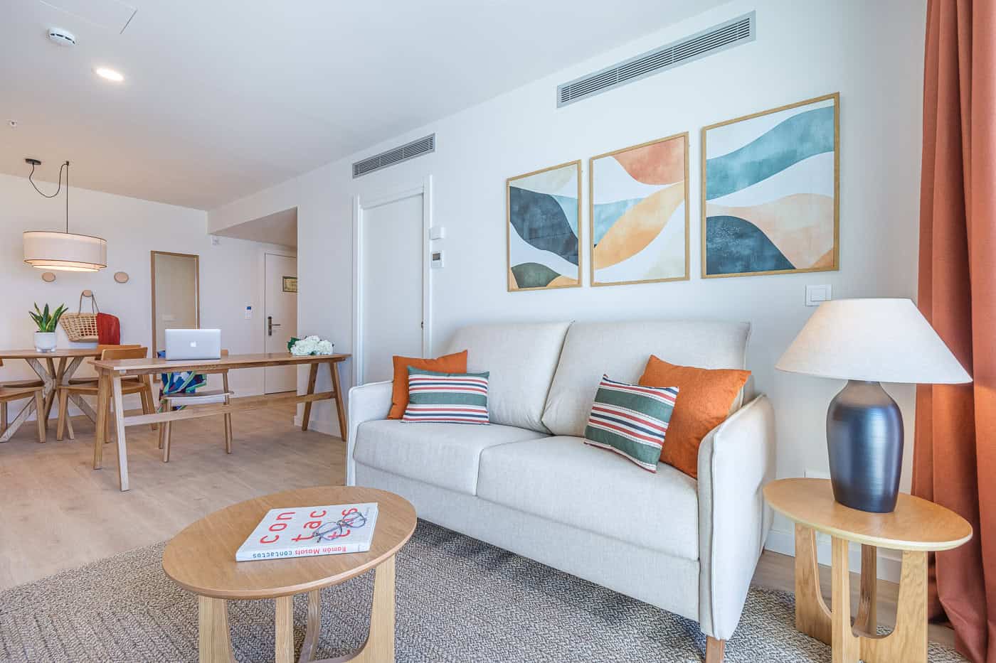 Sala de estar moderna con sofá, cuadros abstractos y lámpara de mesa en tonos cálidos.